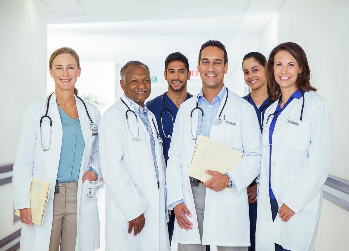 En un plano cerrado se ven 6 médicos, 3 hombres y 3 mujeres sonriendo.