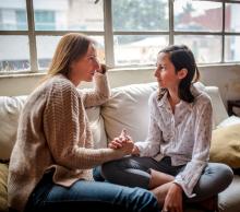 Hay una mujer y una adolscente sentadas frente a frente en un sillón mirándose a los ojos, la mujer tiene sostenida la mano de la adolscente.